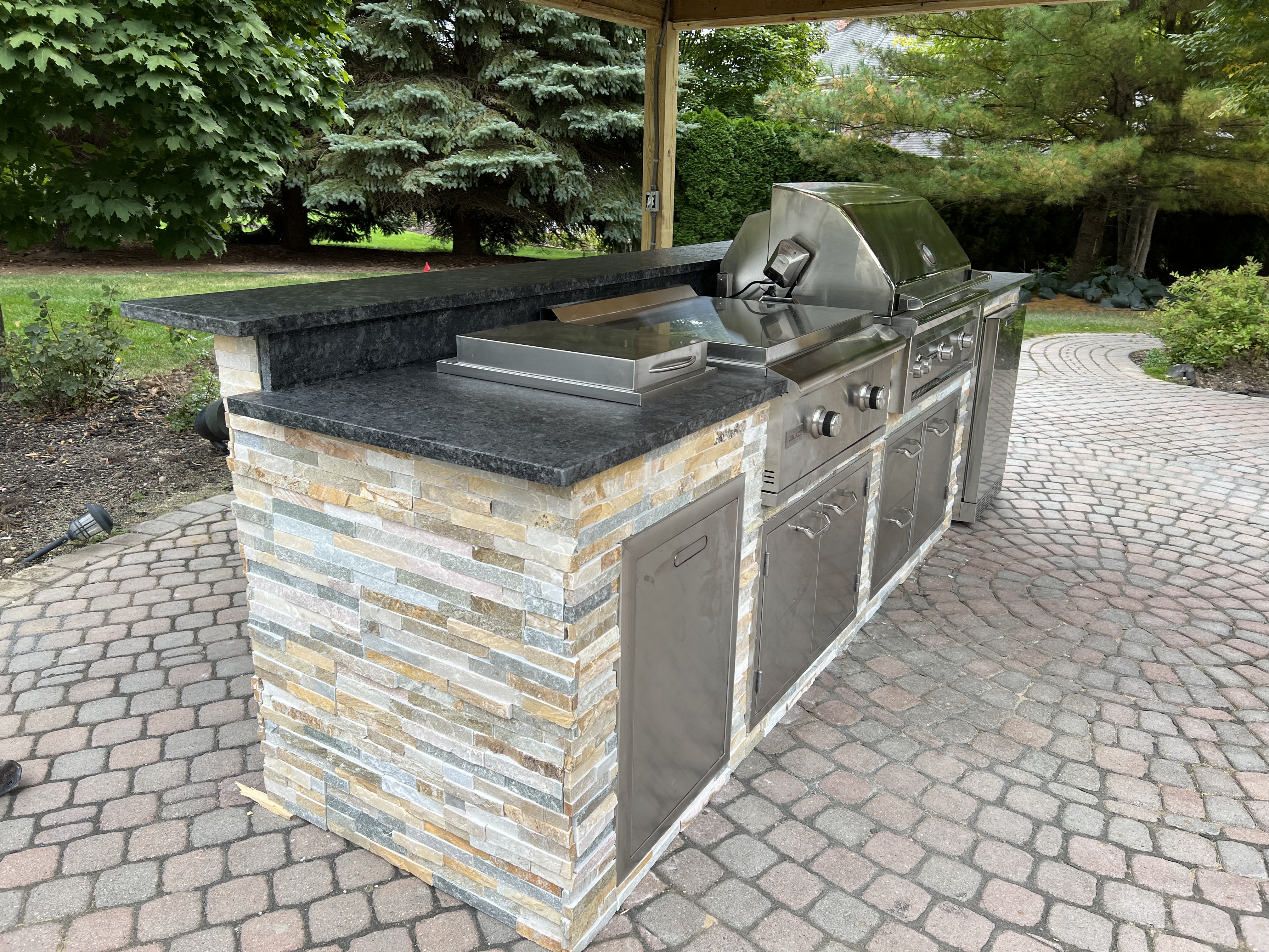 Modern outdoor kitchen with stainless steel appliances and stone countertops.