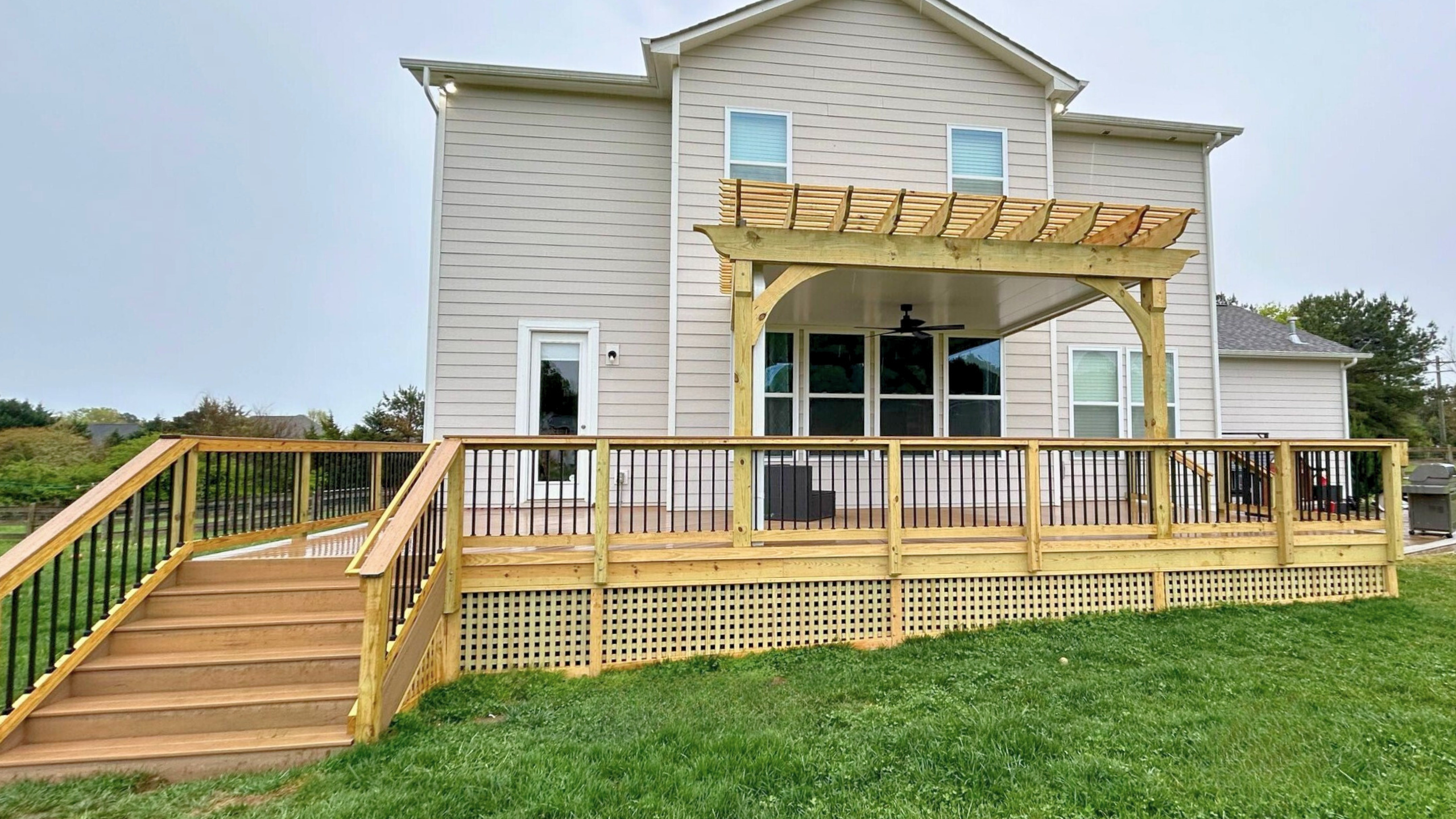 Expansive composite deck with wood skirting, rails, and pergola built by Archadeck of Charlotte.