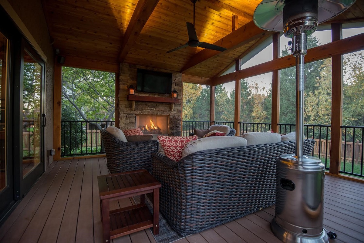 Screened porch with wood vaulted ceilings, weaved outdoor furniture, stone fireplace, and a tv on stone fireplace