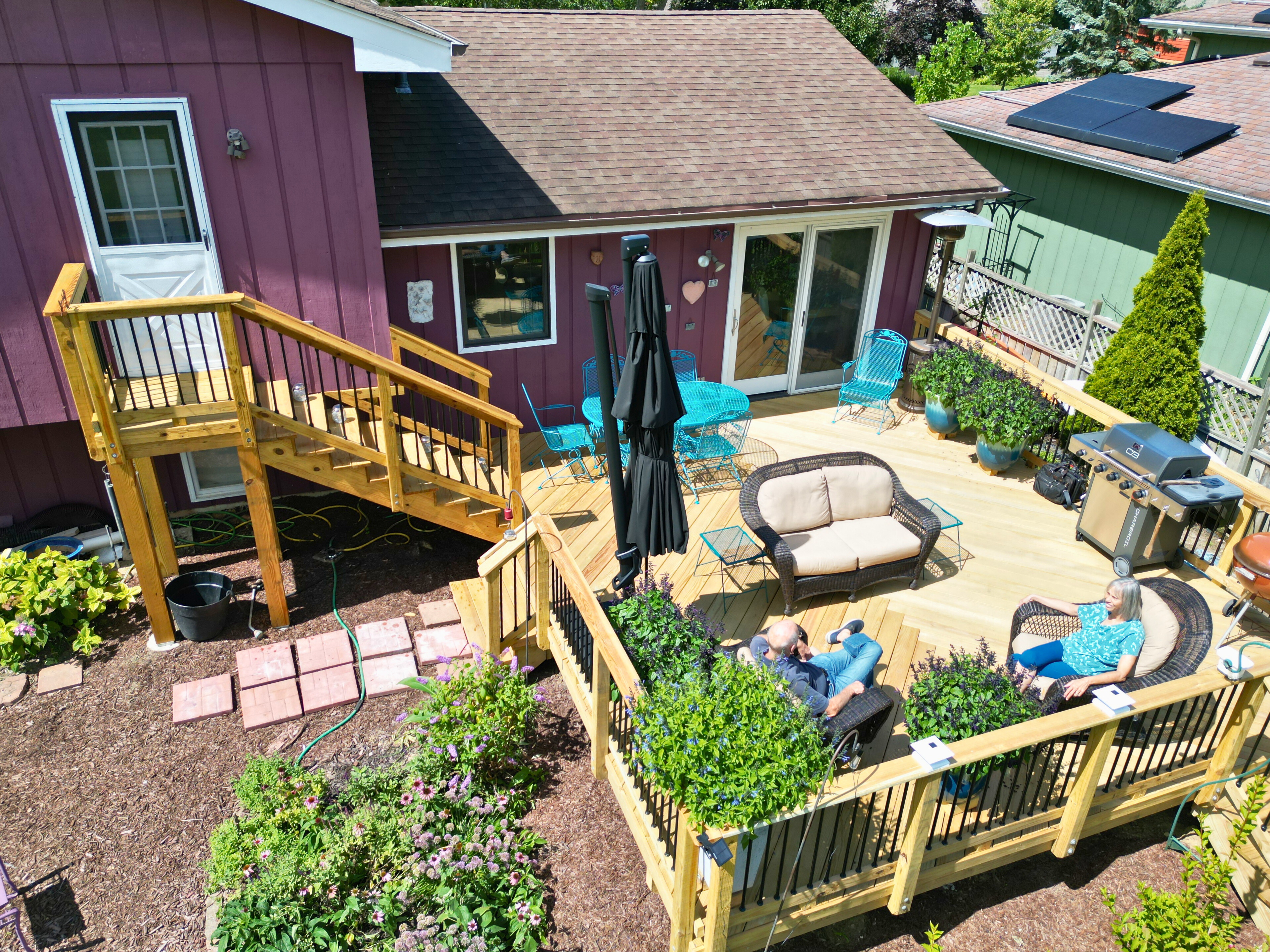 Multi-level wood deck with outdoor furniture, blue lounge chairs, a grill, and greenery in West Chicago,IL.