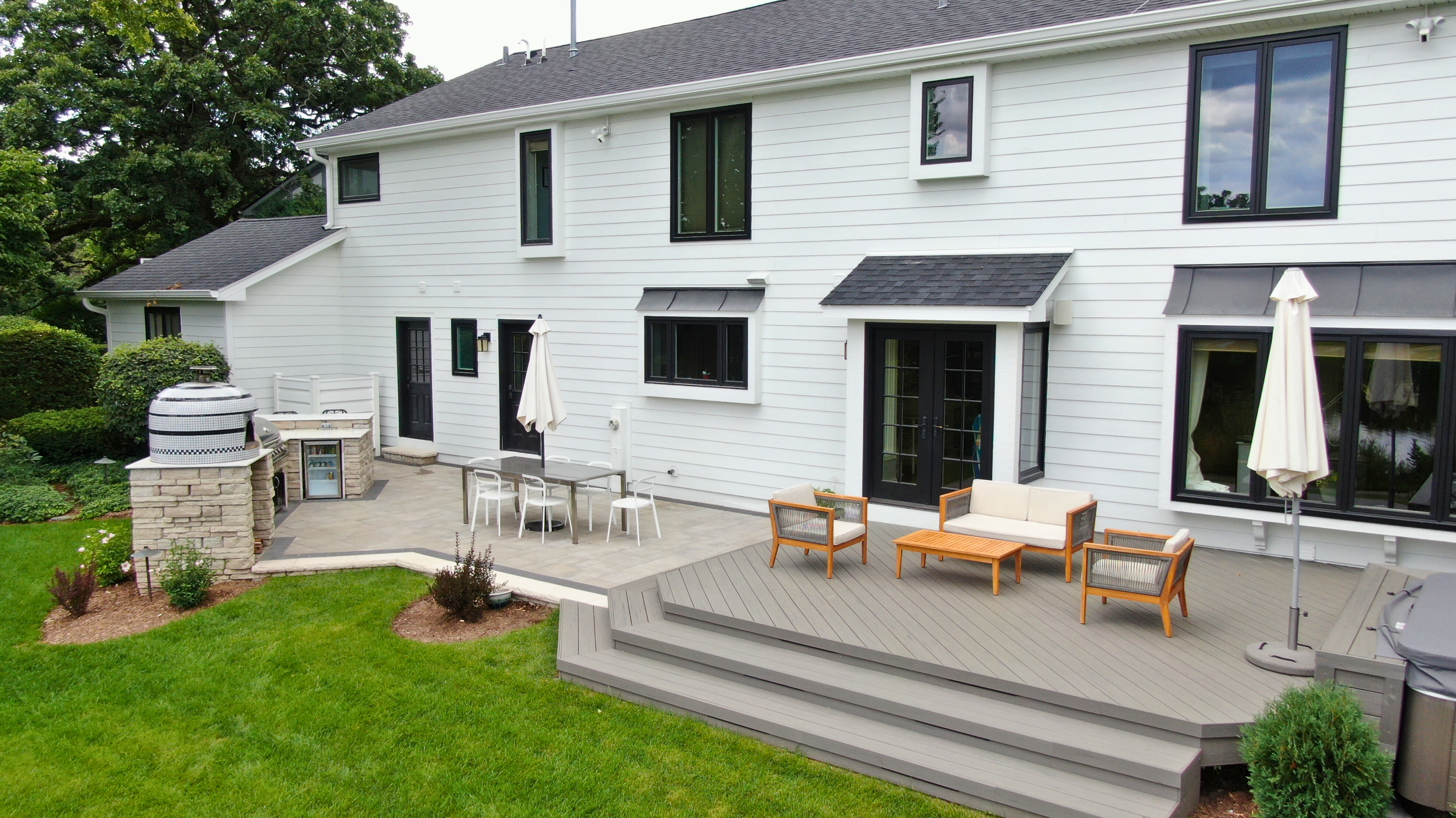 White house with a gorgeous paver patio, otudoor kitchen, pizza oven, and composite deck in lisle, IL backyard. 
