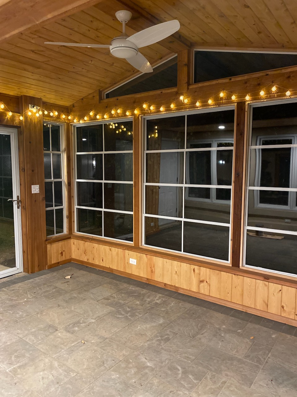 Inside of a custom patio enclosure with vinyl 4-track windows and string lights.
