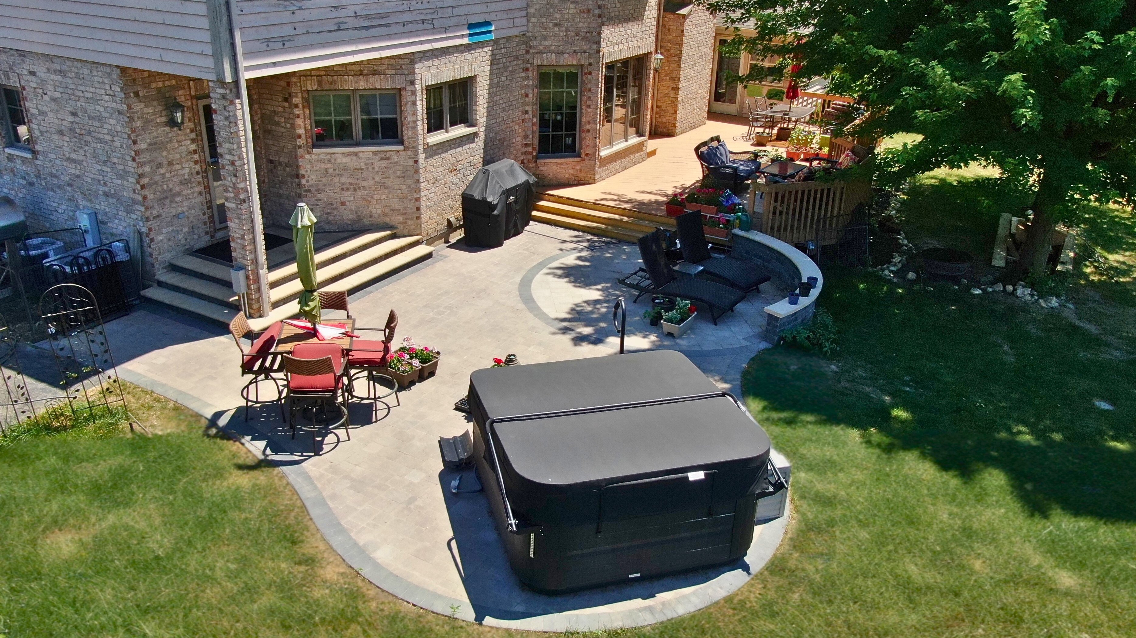 Custom paver patio installation by Archadeck of Chicagoland with a hot tub and a step up to a wood deck.