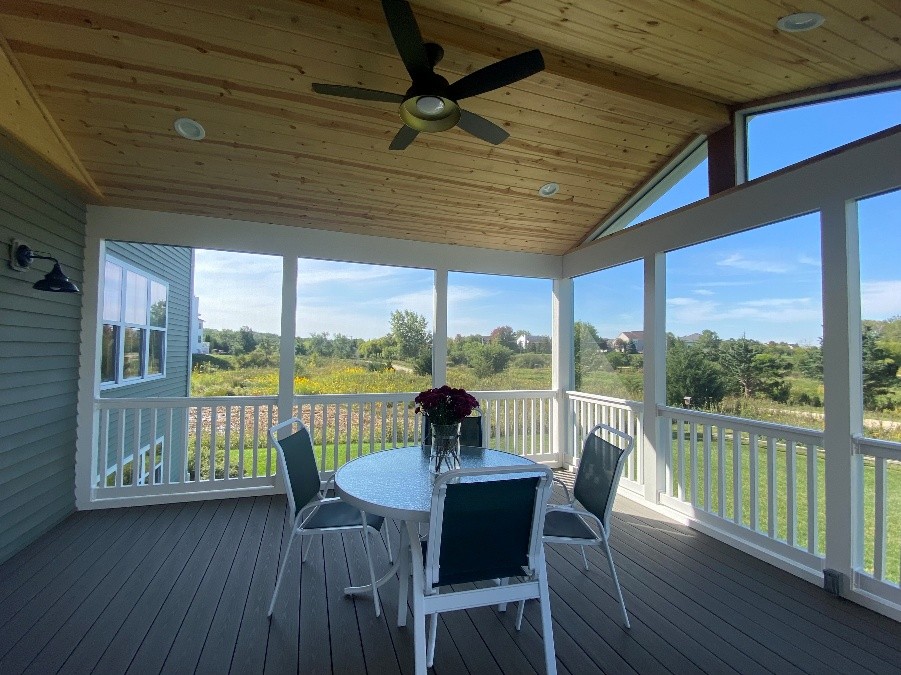 Screened porch with composite decking, vaulted wood ceiling, ceiling fan, and white railing, offering unobstructed views of the Chicagoland landscape.