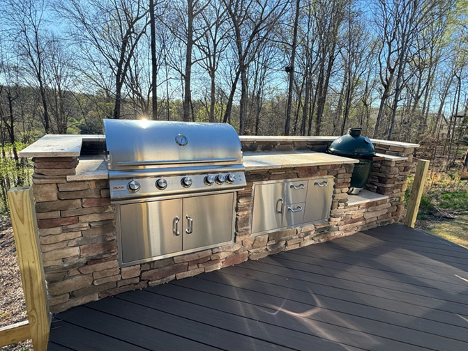 Custom stone outdoor kitchen with built-in Big Green Egg smoker on a large flagstone patio in a Charlotte backyard.