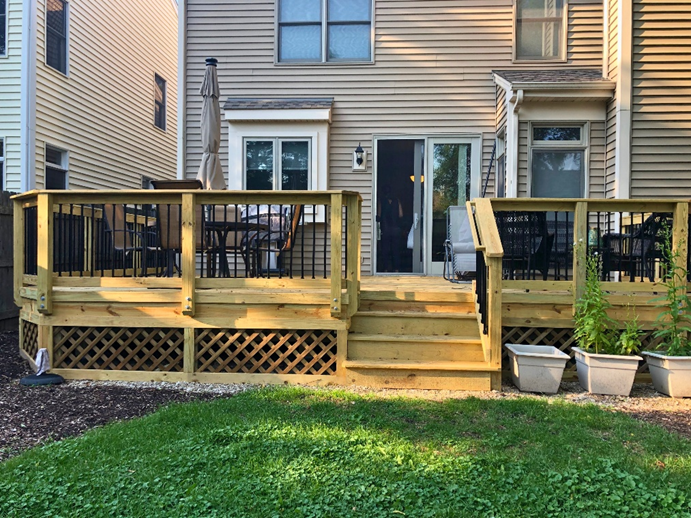 Backyard wood deck in Lake Zurich with steps, black railings, and lattice skirting underneath.