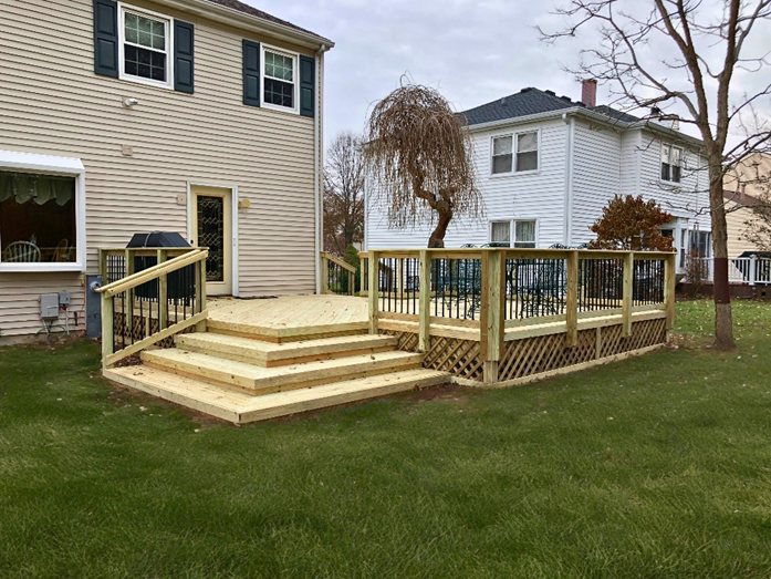 Multi-level wood deck in Lake Zurich, Illinois, with wide stairs, black metal railings, and lattice skirting, attached to a beige house.