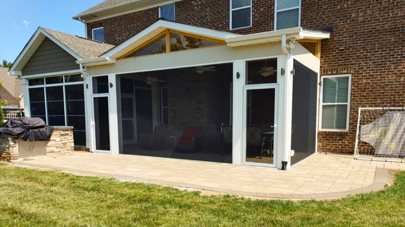 A large, modern screened porch with white trim and a gabled roof extension, built onto a brick home, with an adjacent paver patio and an outdoor kitchen area, in Mint Hill, NC.