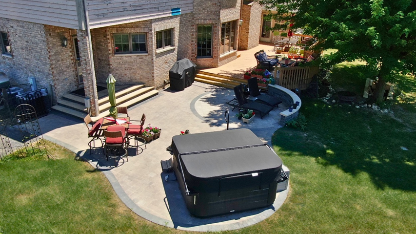 Aerial view of a large backyard patio in Homer Glen with a black hot tub, an oval paver patio, and outdoor furniture.