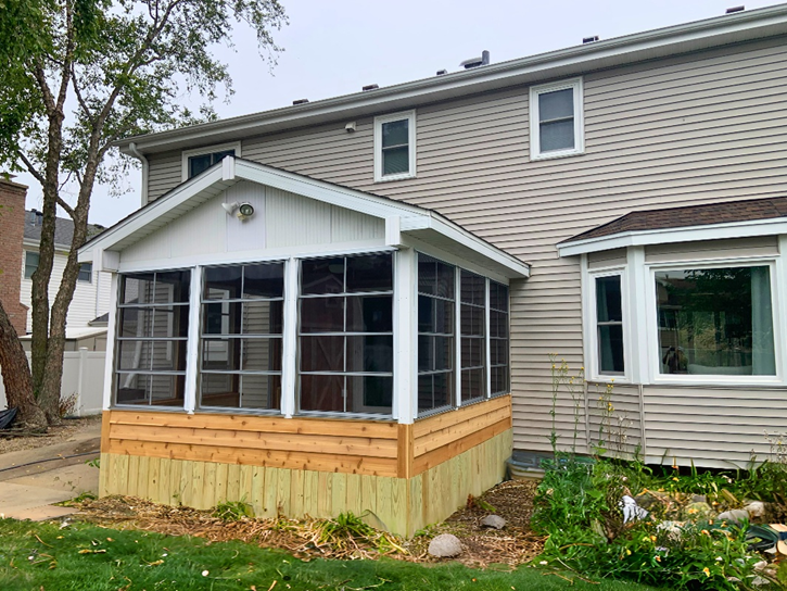 New three-season room addition on the back of a Lake Zurich home, with large windows and wood siding