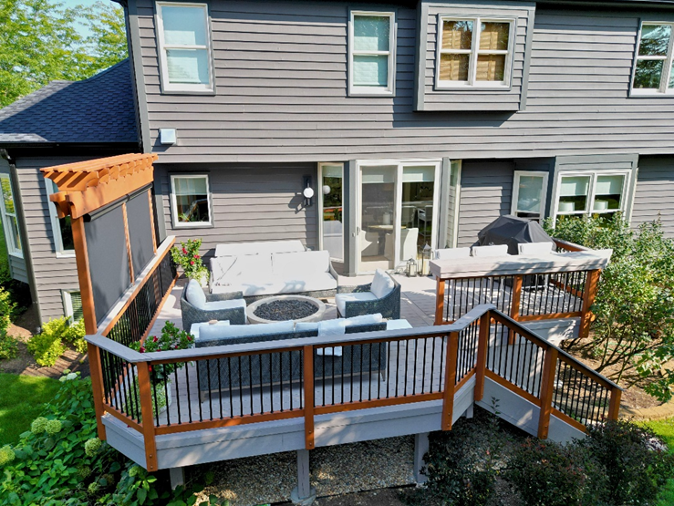 A contemporary low-maintenance TimberTech deck with dark grey planks and black metal railings, leading down to a green lawn, attached to a light-colored vinyl-sided house in Geneva, IL. Outdoor furniture with blue cushions is visible on the deck.