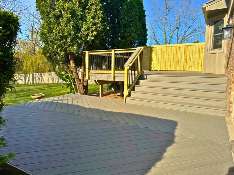 Multi-level TimberTech composite deck in light grey, featuring diagonal decking patterns, natural wood railings with black balusters, and a privacy fence in a Homer Glen backyard.