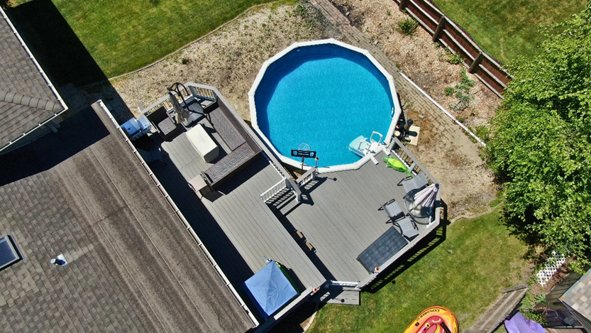 Overhead view of a large TimberTech composite deck in varying shades of grey built around an above-ground swimming pool, with outdoor seating areas and a grill.