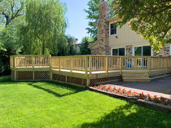  large, multi-level wooden deck with natural wood railings and lattice skirting, extending across the back of a brick house with a green lawn.