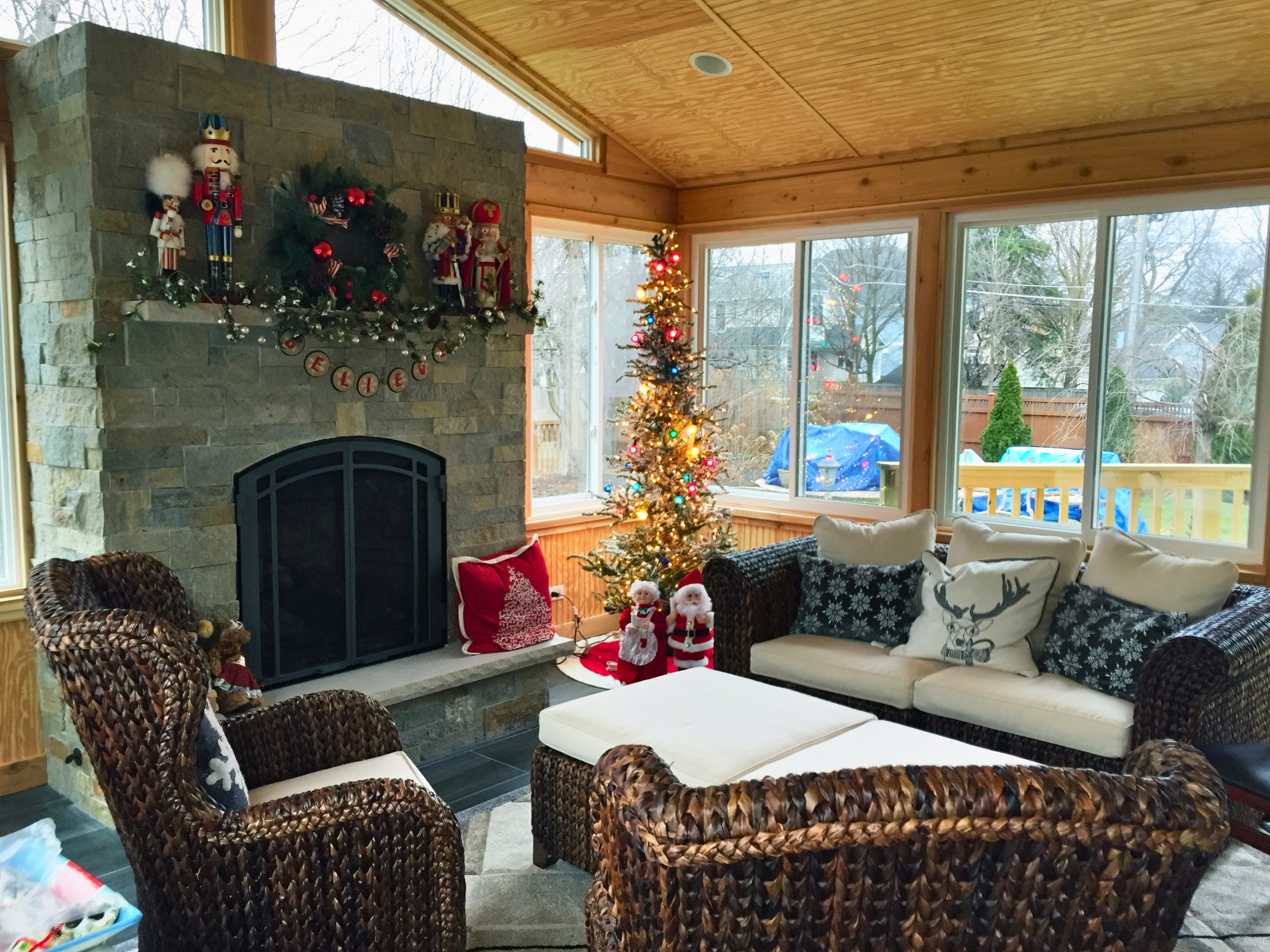 Inside of an Archadeck sunroom with a stone fireplace, outdoor furniture, decorated for Christmas.