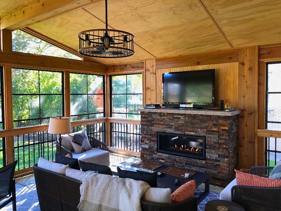 Inside of a three season room with a stone fireplace, 4-track windows, and cozy furniture in Barrington, IL.