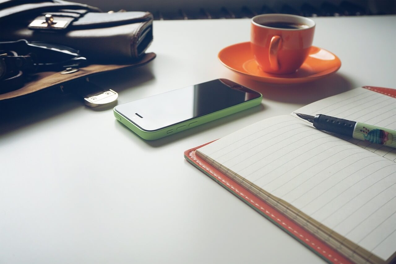Table with phone, cup of coffee, wallet and journal