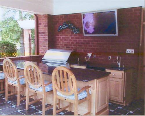 This covered patio space features an outdoor kitchen with bar seating and a wall-mounted TV