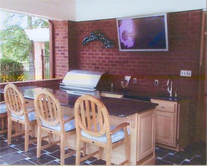 This covered patio space features an outdoor kitchen with bar seating along with a wall mounted TV