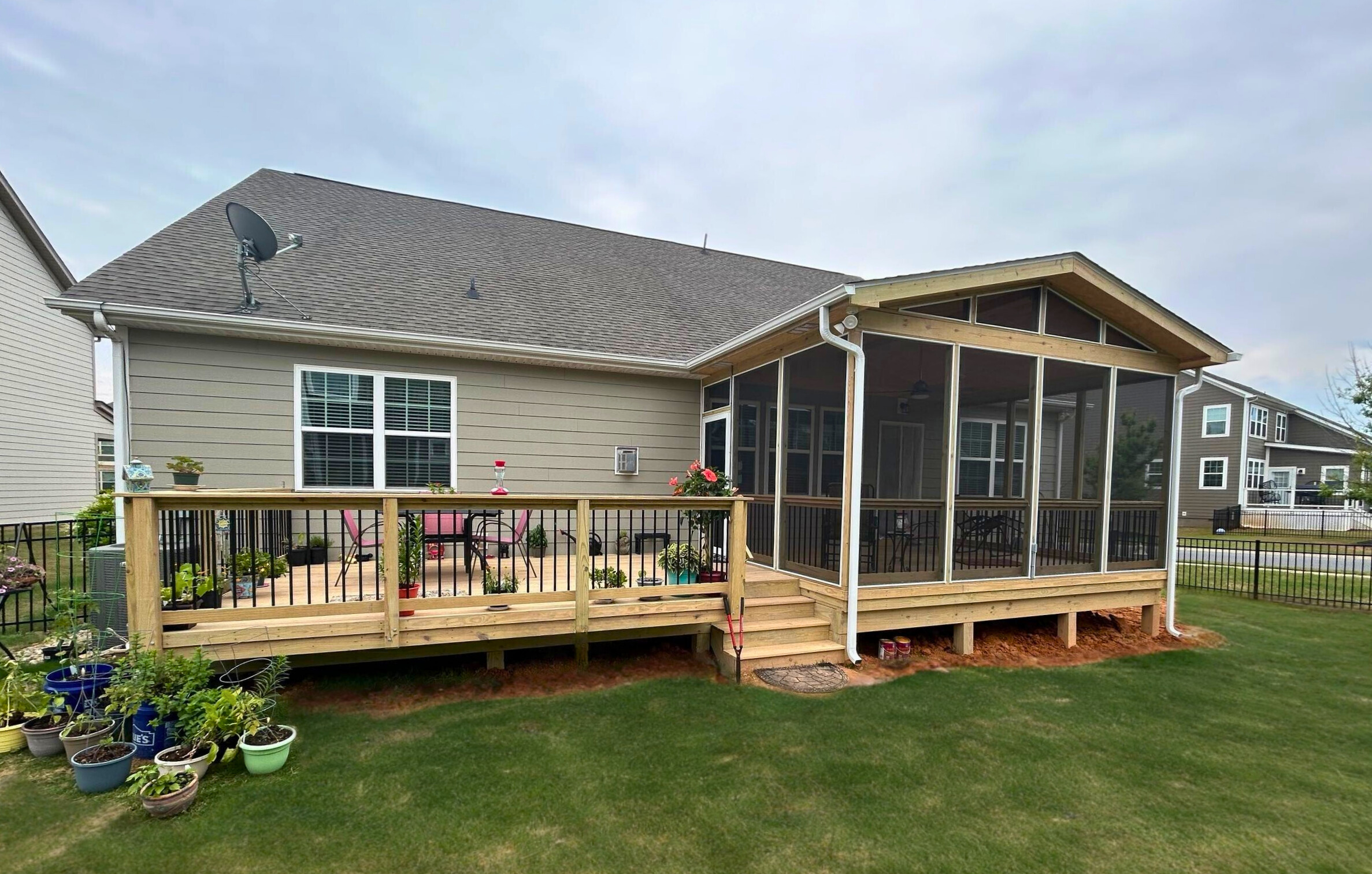 Expansive Indian Land outdoor living space featuring a new wooden deck and a screened porch addition on a tan siding home."