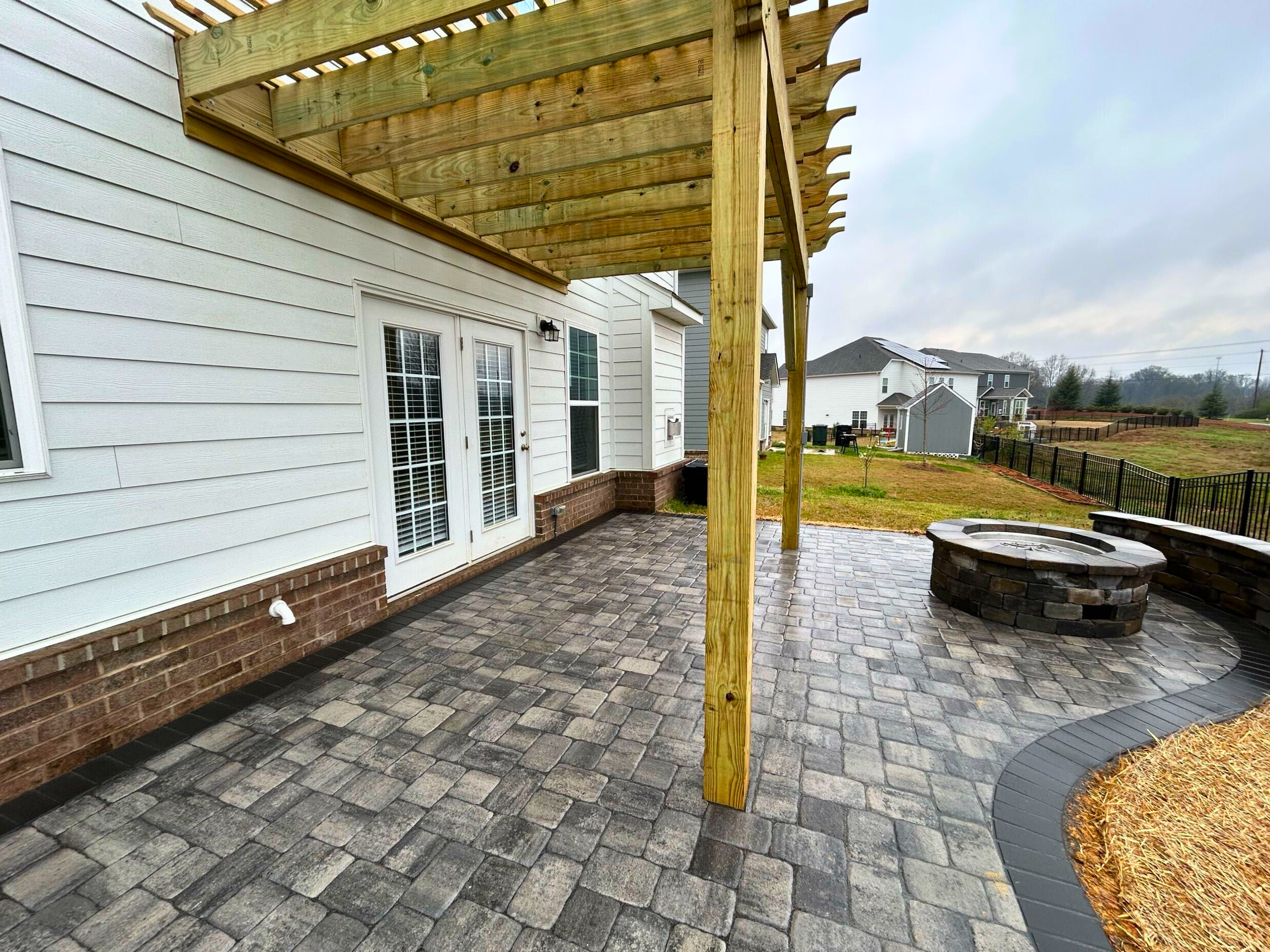 Custom paver patio with built-in fire pit and wooden pergola, ideal for outdoor gatherings at an Indian Land home.