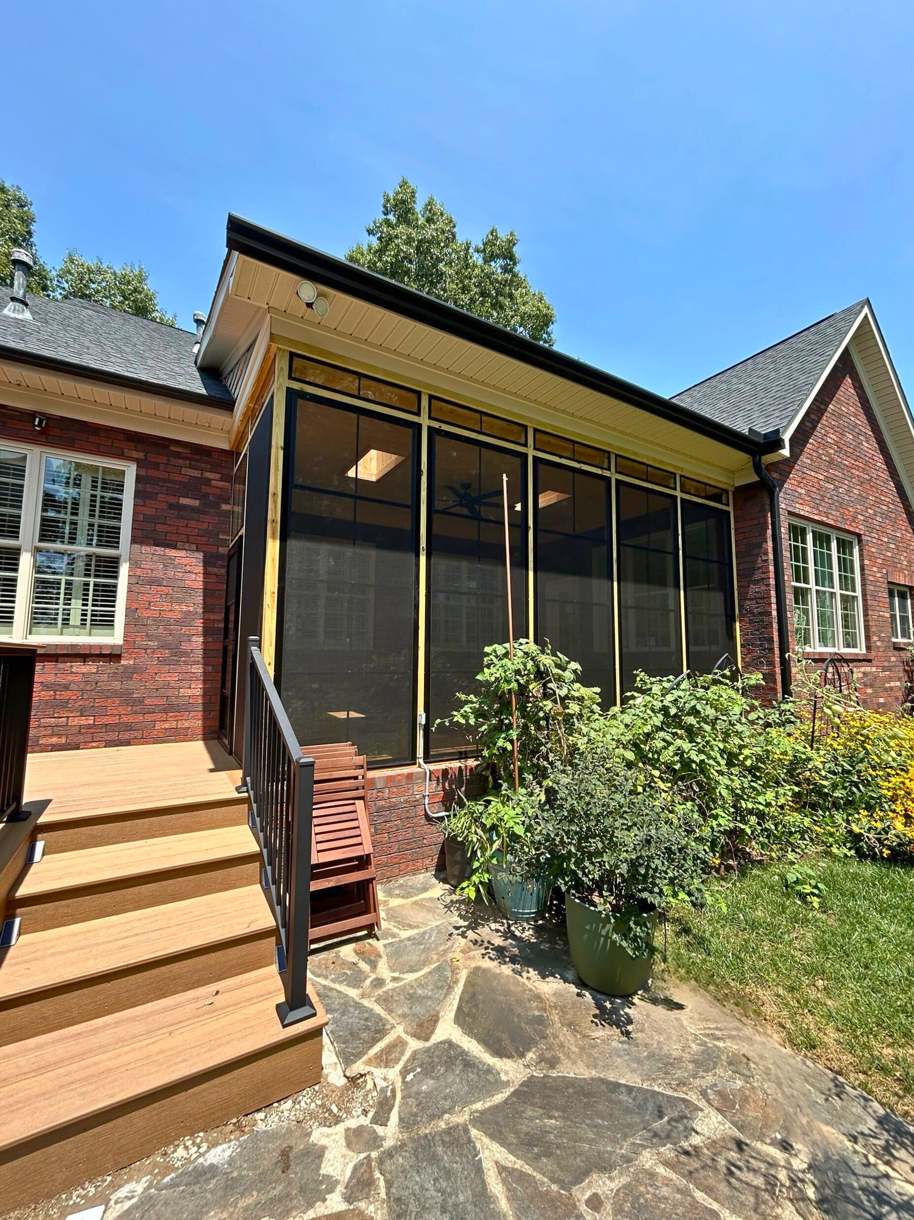 A traditional brick home in Davidson, NC, with a newly constructed screened porch featuring a stone patio and steps leading to a wooden deck.