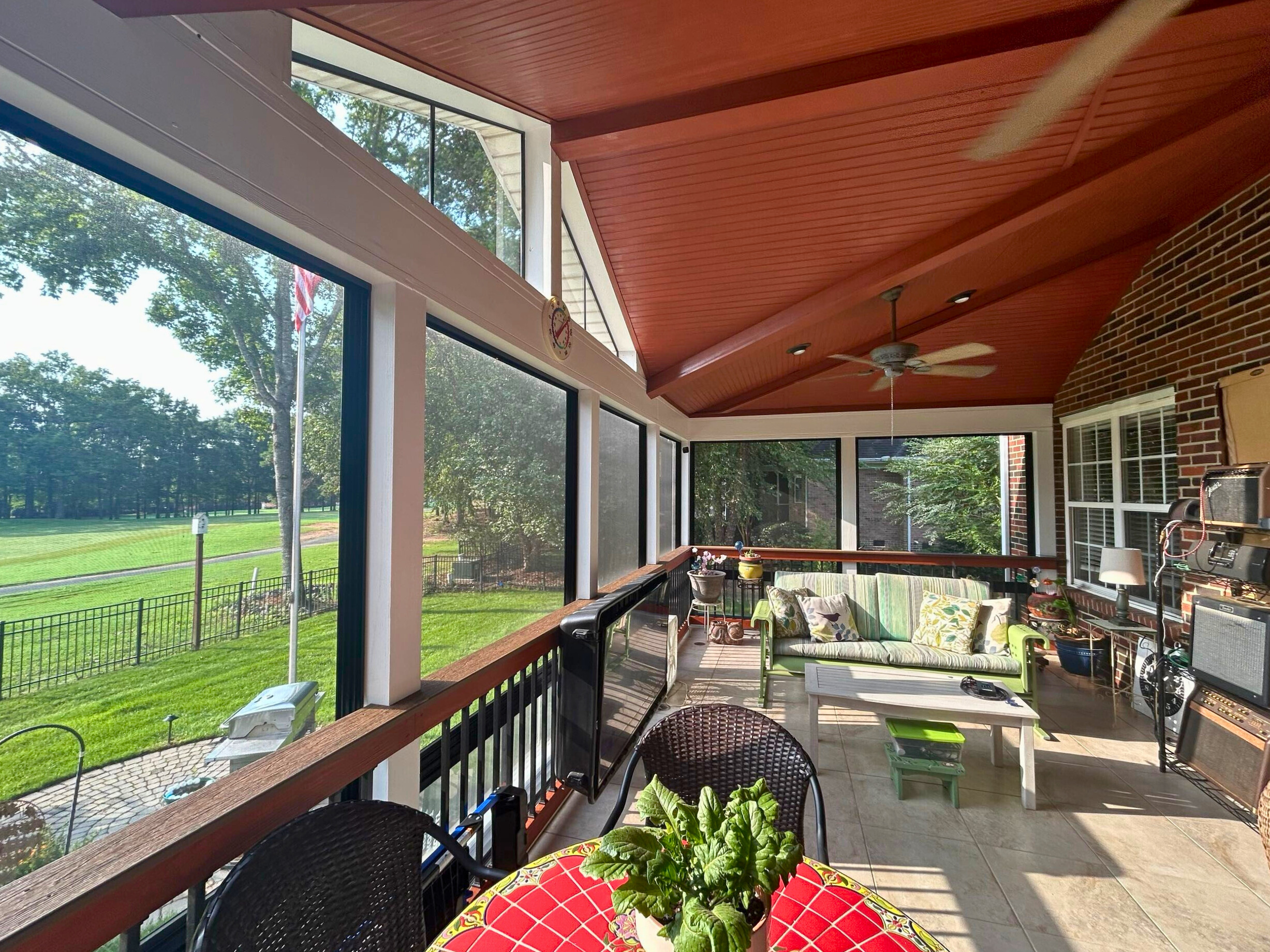 Interior of a large screened porch in Matthews, NC, featuring a vibrant red ceiling, comfortable outdoor furniture, and a clear view overlooking a golf course.