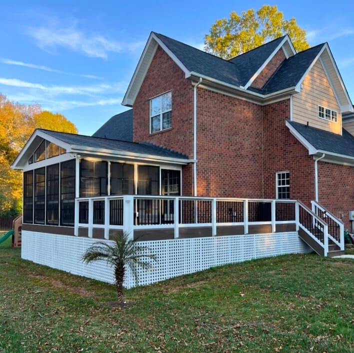 Composite deck with white lattice and black railings connected to a screened porch on a brick home in Monroe NC, built by deck and porch builders.