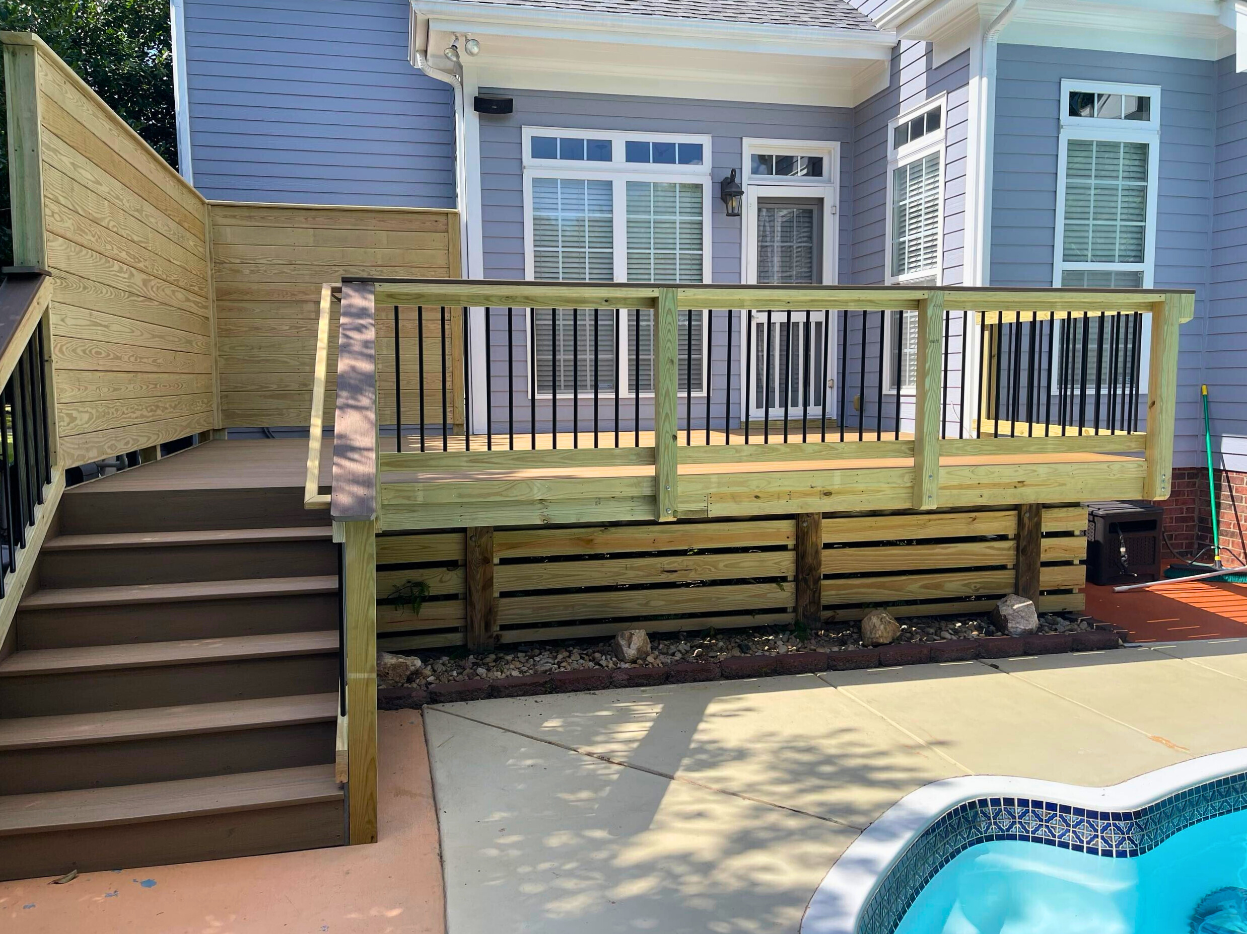 New composite deck with wood skirting and black balusters next to a swimming pool in Tega Cay