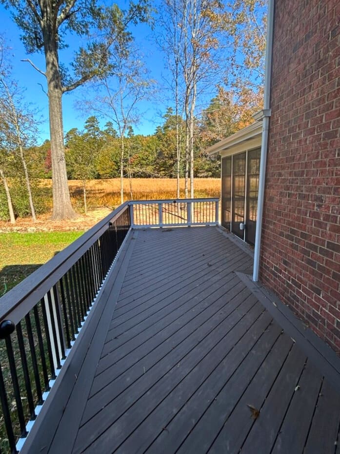 Long, dark composite deck with black railings extending alongside a brick home, overlooking a field in Monroe NC.