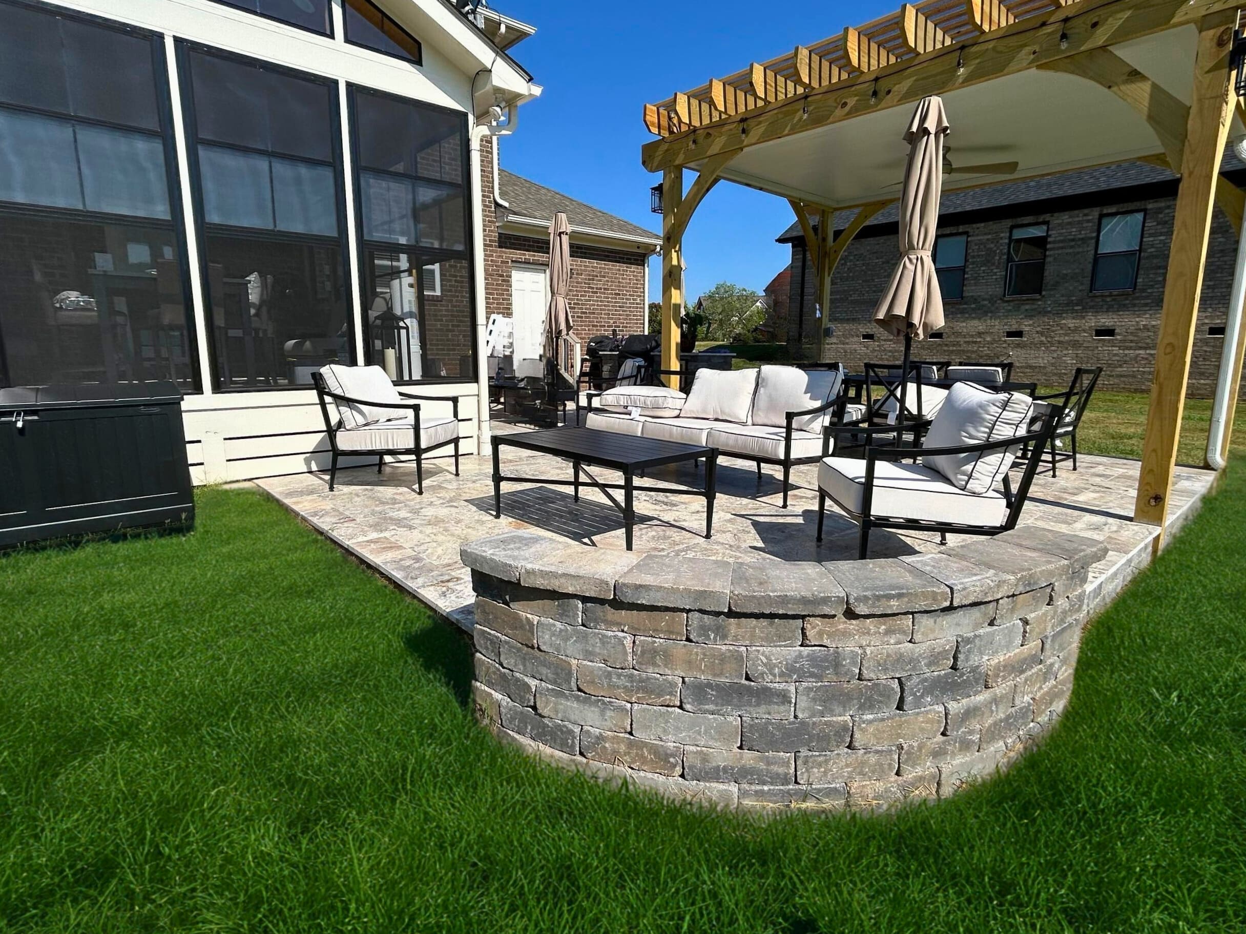 Large paver patio with stone retaining wall and a wooden pergola, installed by a paver patio builder in Monroe NC.