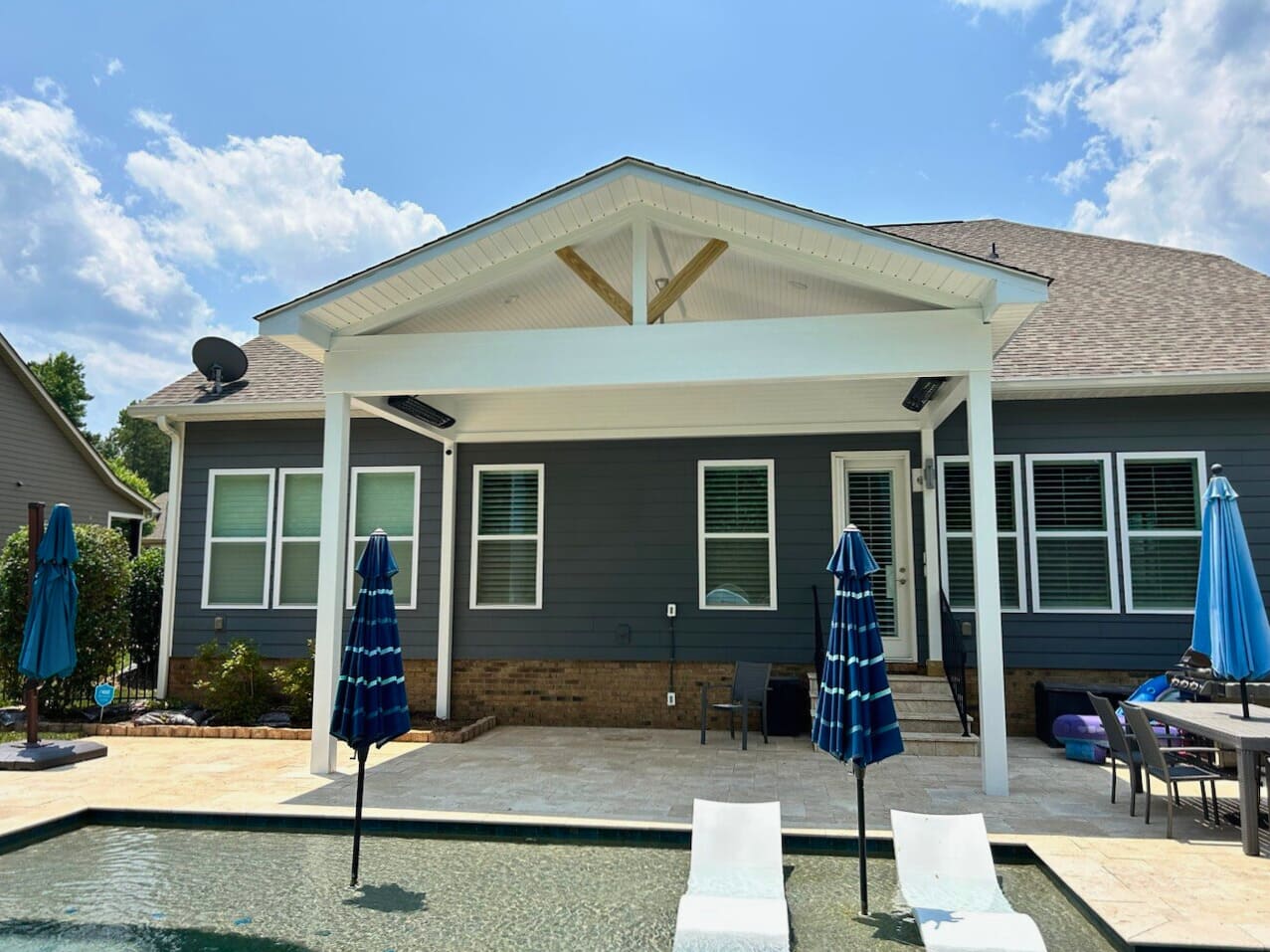 Custom-built covered porch with a high ceiling, overlooking a swimming pool in a backyard in Monroe NC, built by porch builders.