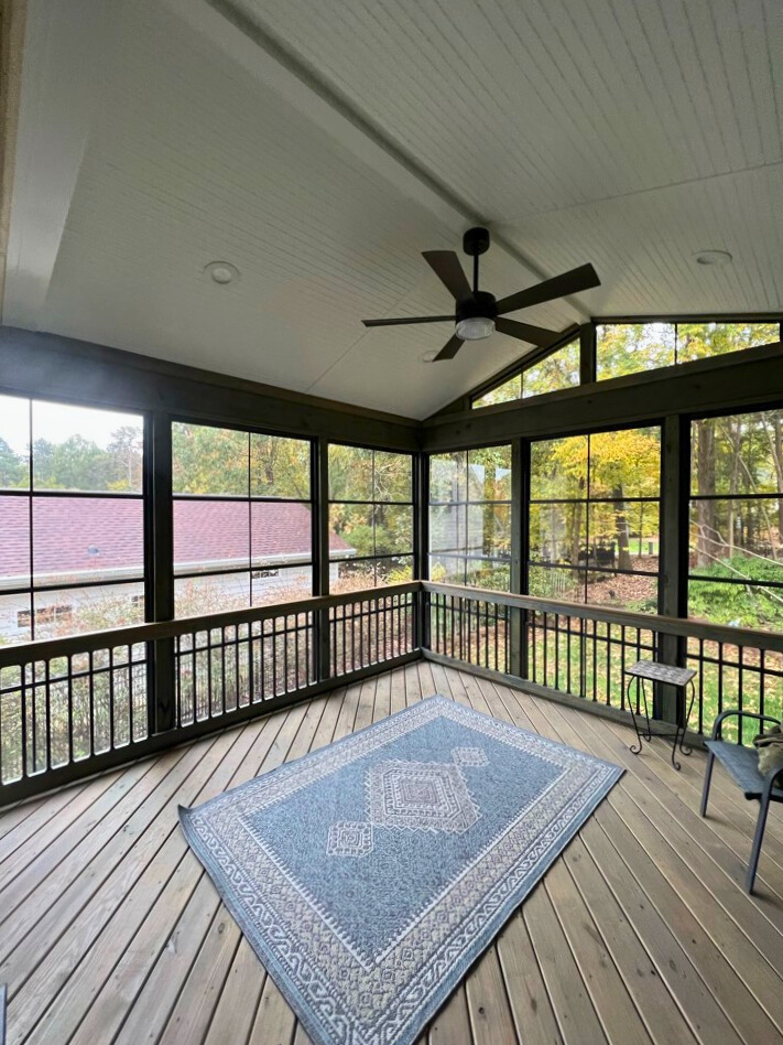 Interior view of a modern Indian Land three-season room featuring large windows, a ceiling fan, and a wood-look deck floor.