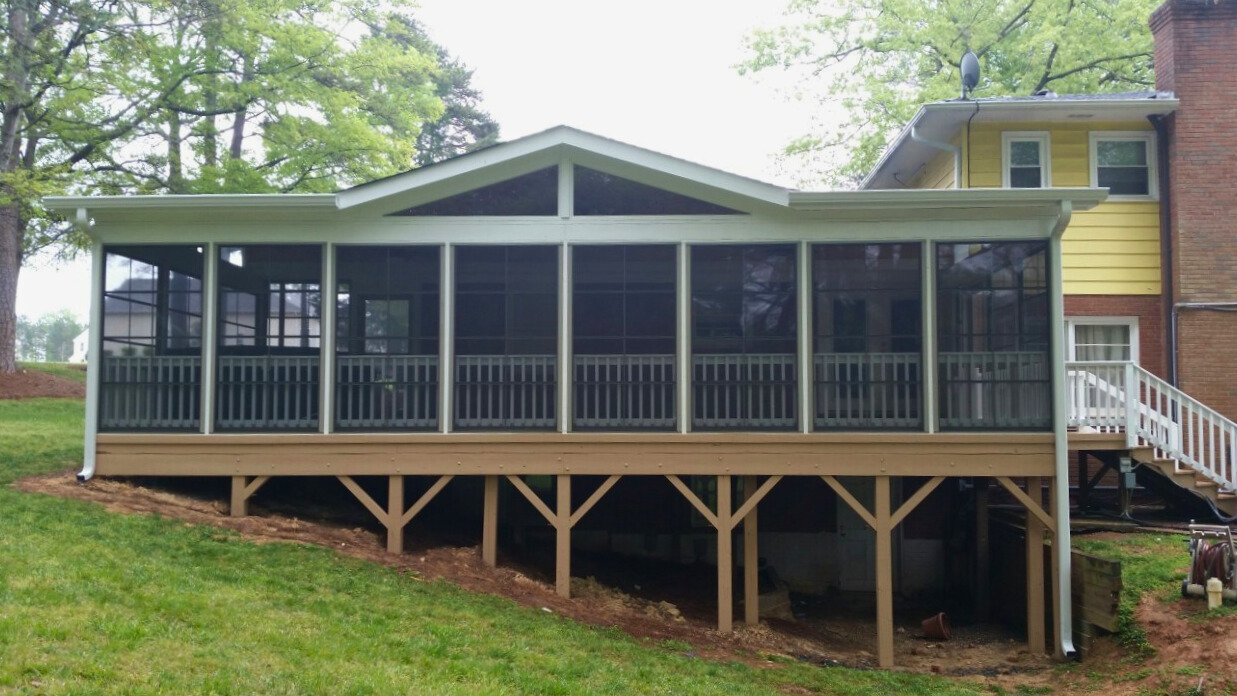 Exterior view of a raised screened porch addition in Matthews, NC, built on a composite deck foundation with stairs leading down to the yard.