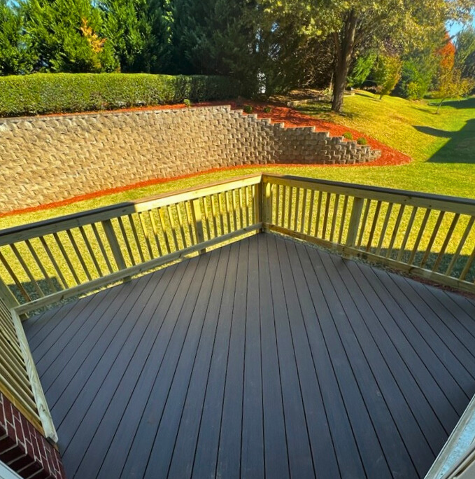 New composite deck with brown decking and wood railings, overlooking a retaining wall in a Waxhaw, NC backyard.