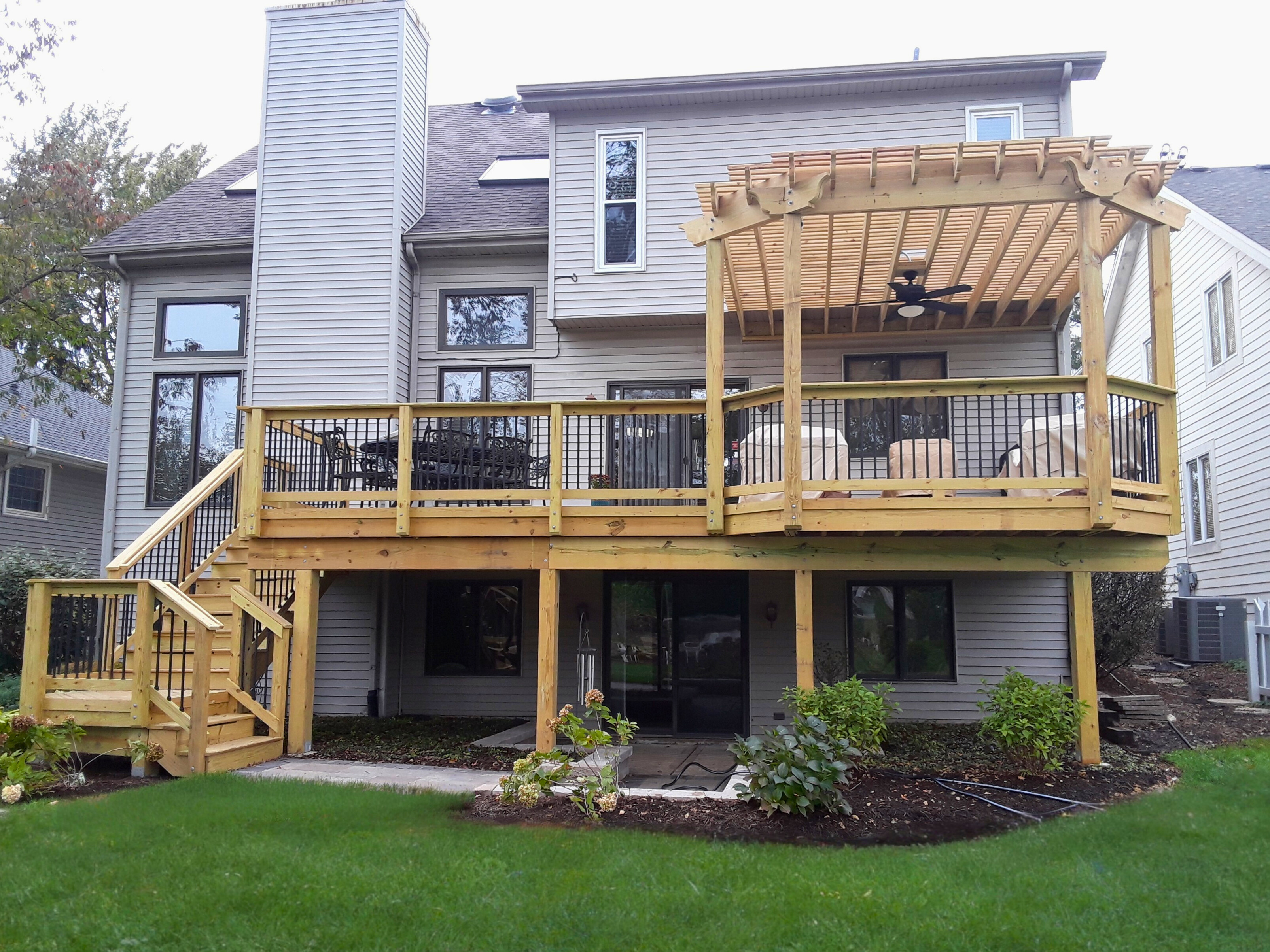 Multi-level custom wood deck with black metal railings and an attached pergola featuring a ceiling fan, built by Archadeck of Chicagoland for a home in Downers Grove, IL.