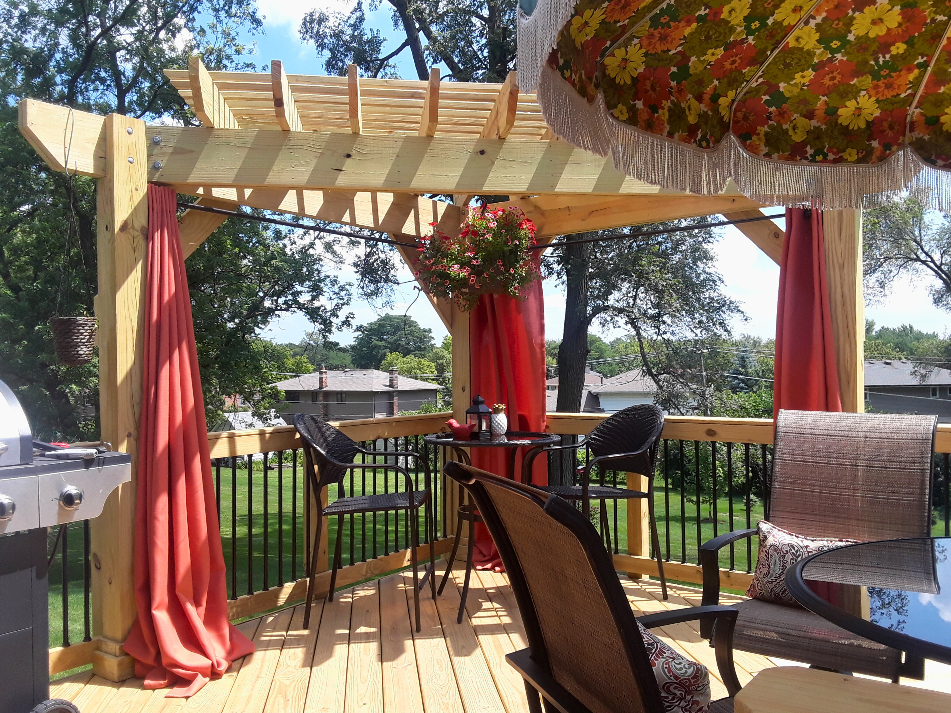 Wooden deck with black railings and a custom pergola featuring red curtains, creating a shaded outdoor dining area in Downers Grove, IL. Deck installation by Archadeck of Chicagoland.