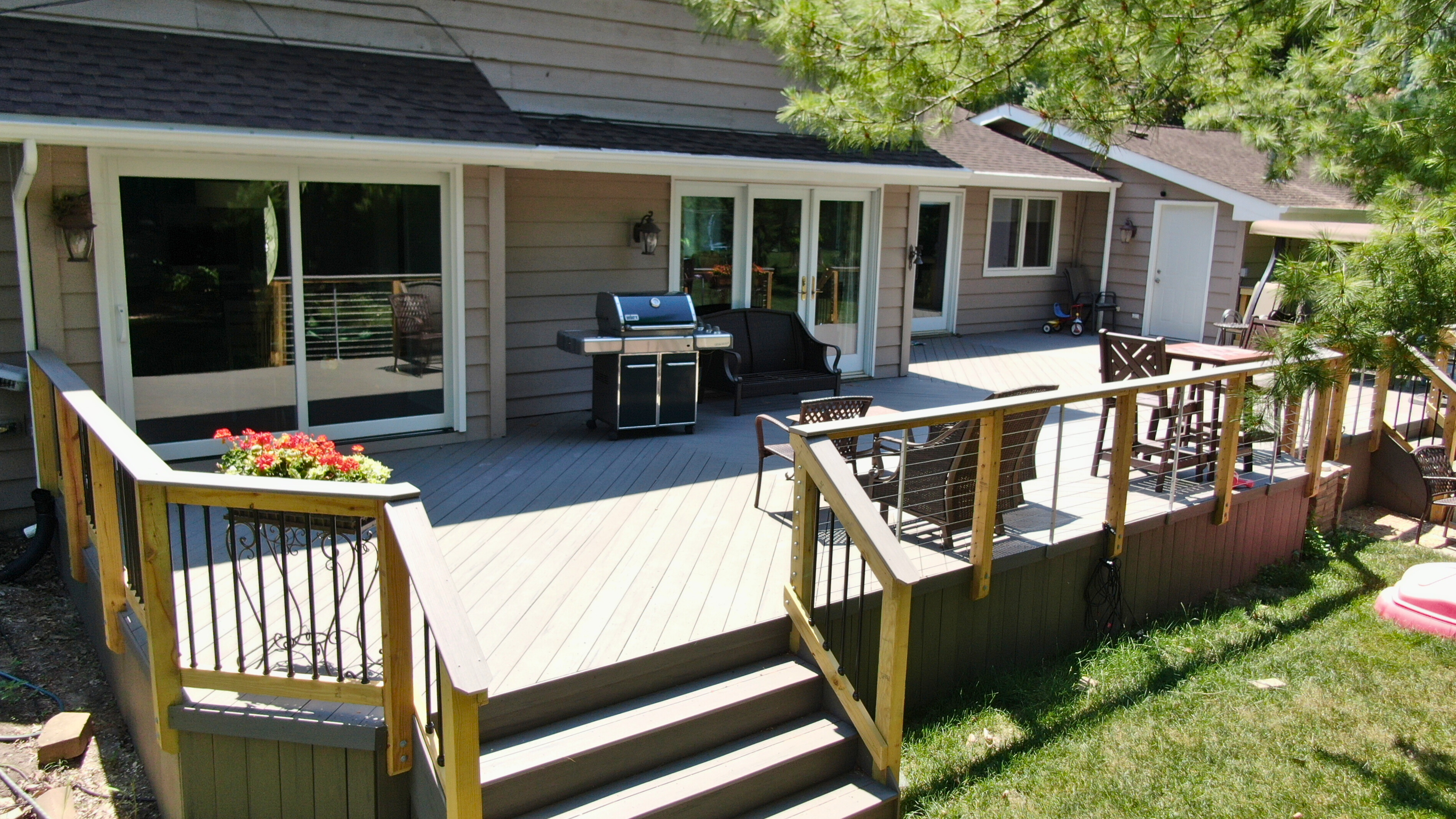 Spacious composite deck in gray tones with steps, black and cable railings, built by a Downers Grove deck builder, Archadeck of Chicagoland. The deck provides ample space for entertaining outside a light brown house.
