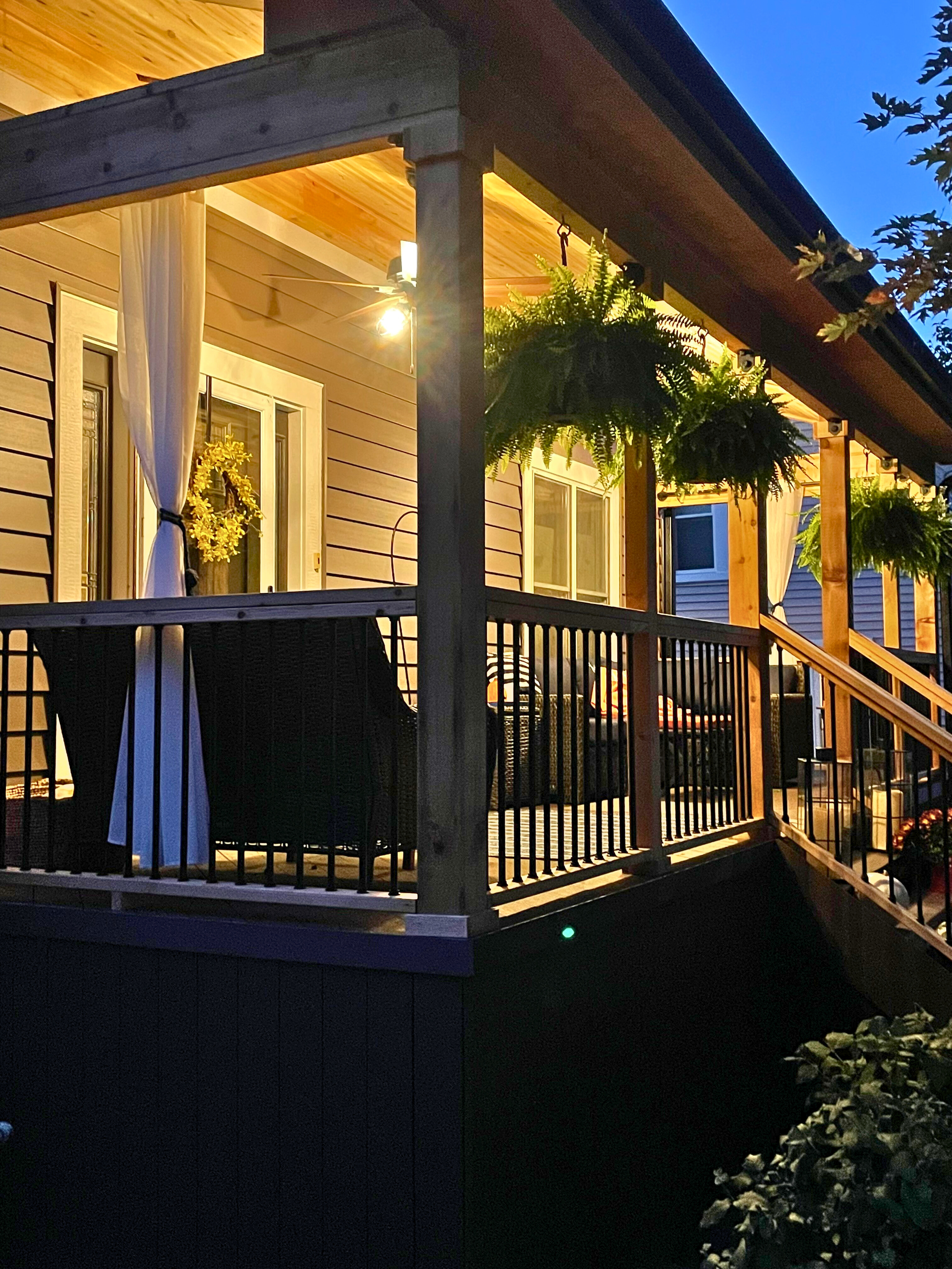 Inviting front porch with a wood ceiling, recessed lighting, and hanging plants, featuring dark railings and comfortable seating, built by Archadeck of Chicagoland in Downers Grove, IL.