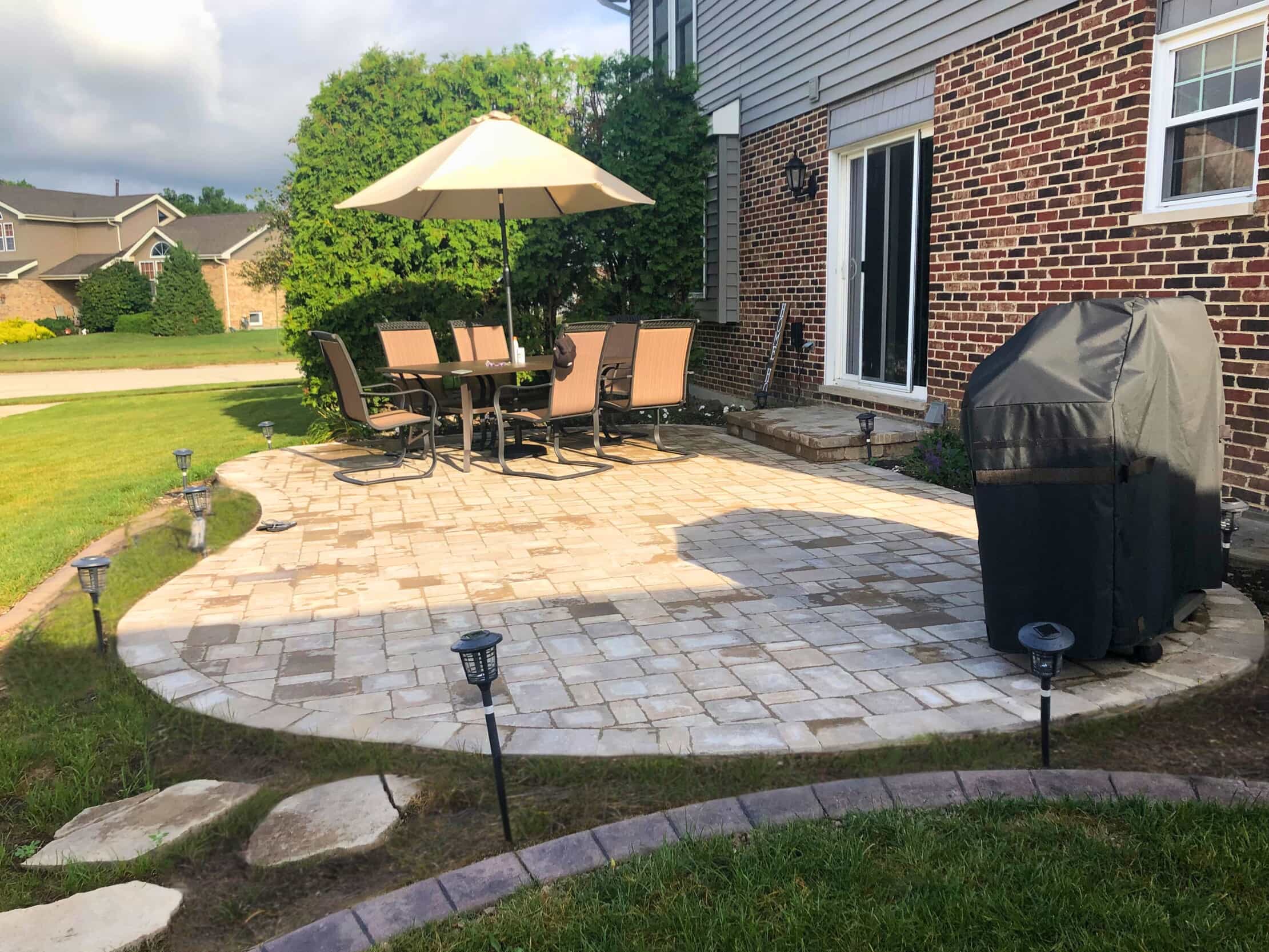 Custom curved paver patio with outdoor dining set and umbrella in a Frankfort, IL backyard