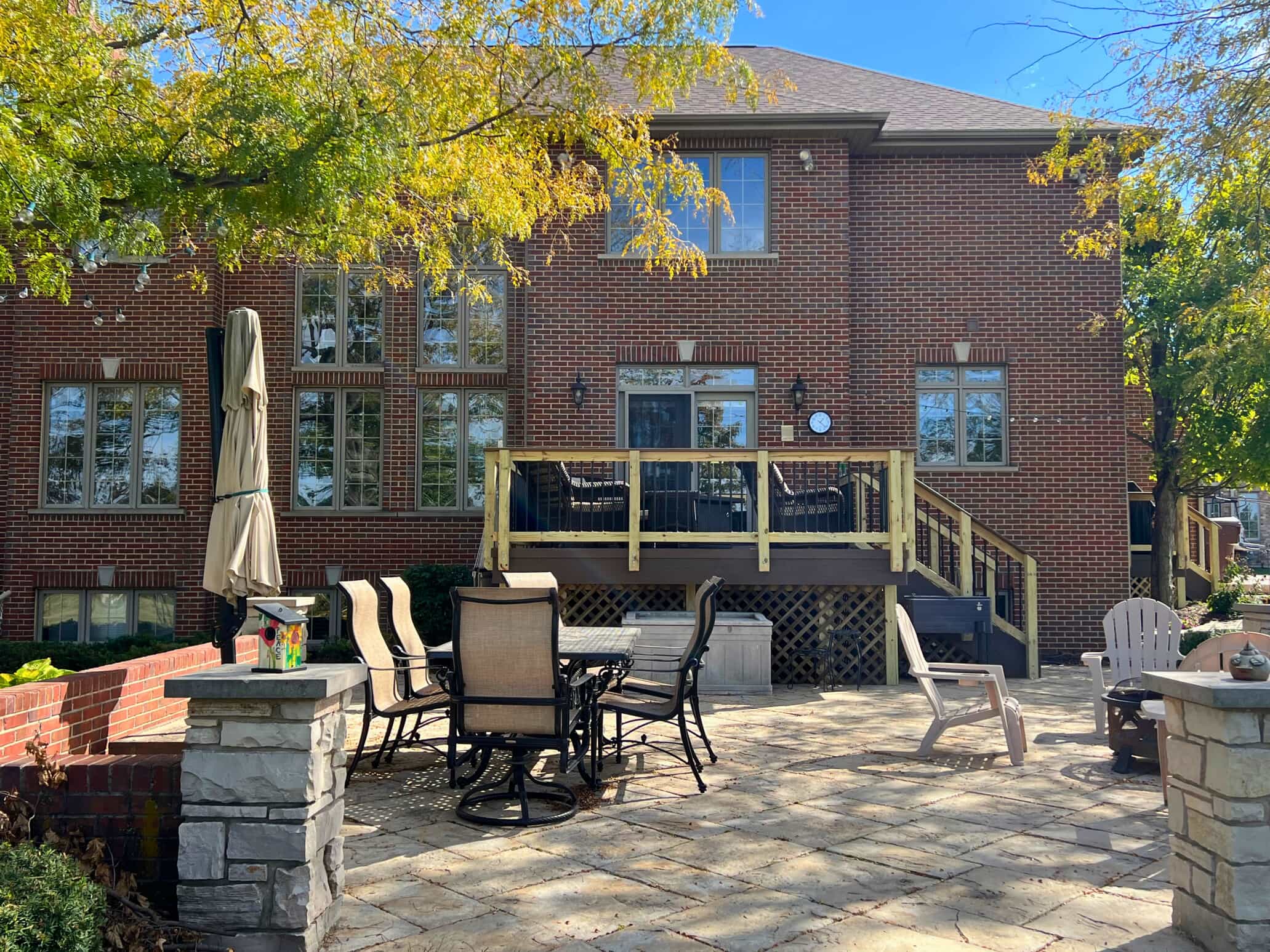 Large stone paver patio with a wood deck and brick pillars on a Frankfort, IL home