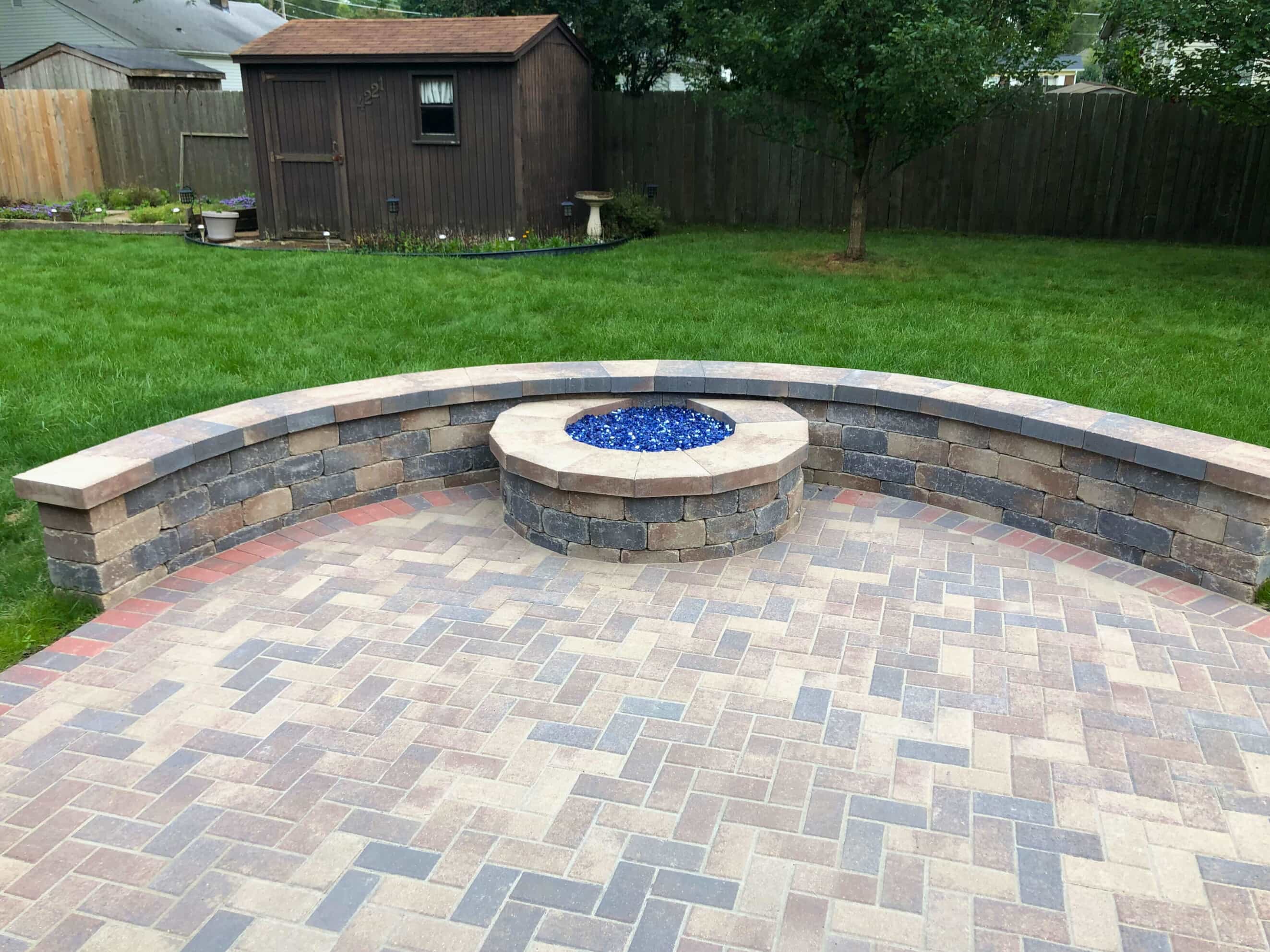 Herringbone pattern paver patio with a curved stone retaining wall and a built-in gas fire pit, surrounded by a green lawn in Tinley Park, IL.