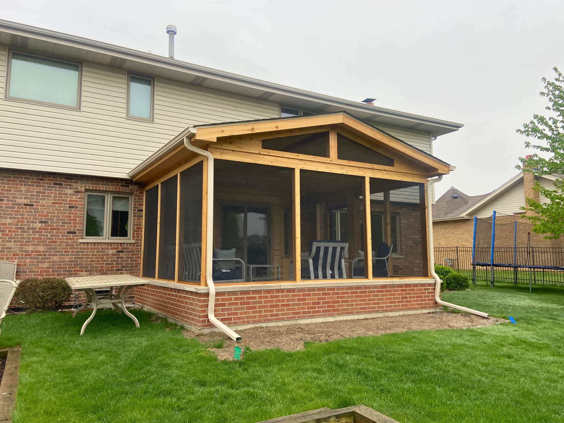 Newly constructed screened porch with a brick base and wood framing attached to a light-colored house in Tinley Park, IL, next to a green lawn.
