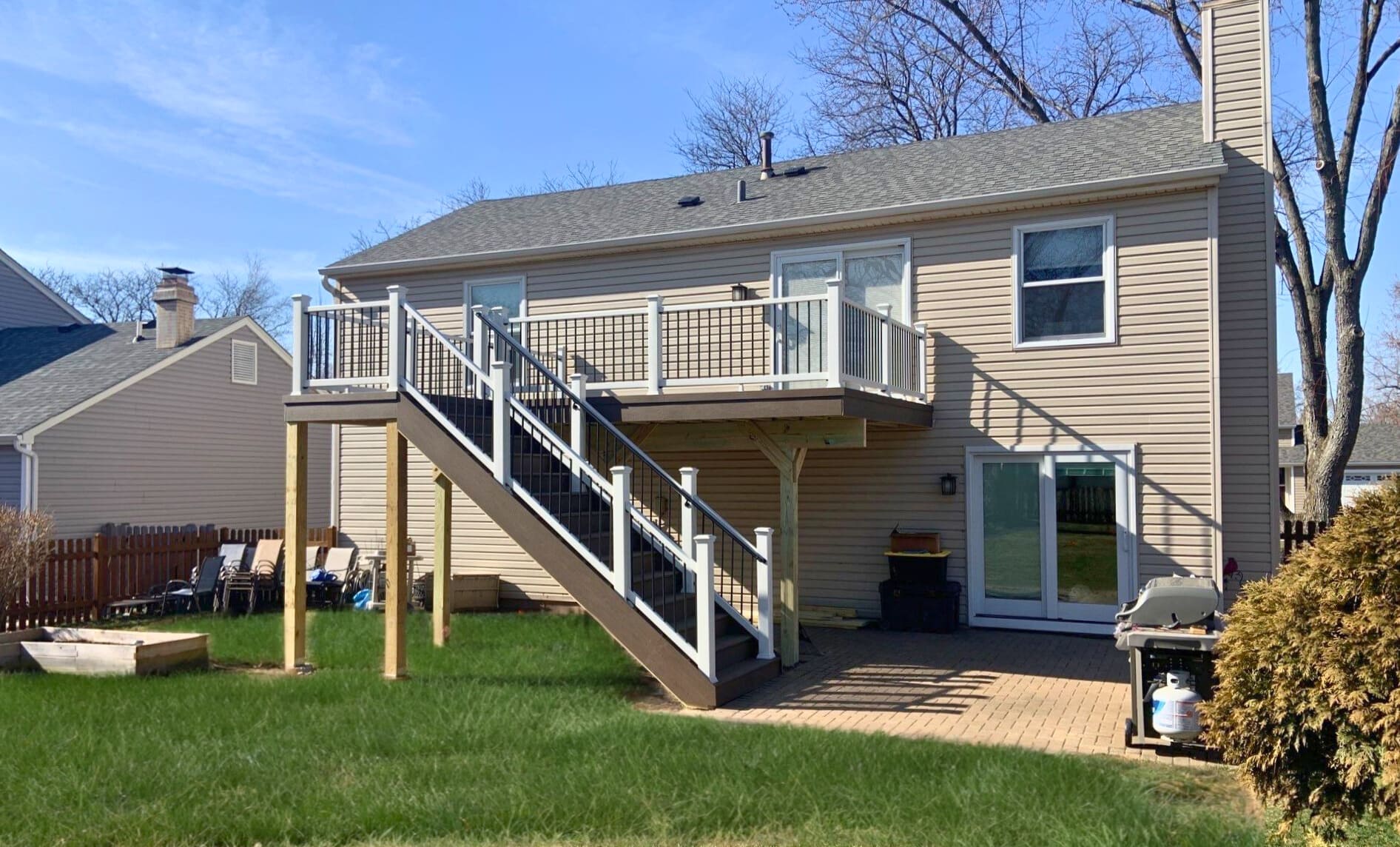 Newly built composite deck in St. Charles, IL, featuring TimberTech decking, white railings with black balusters, and a staircase leading to the yard, attached to a house.
