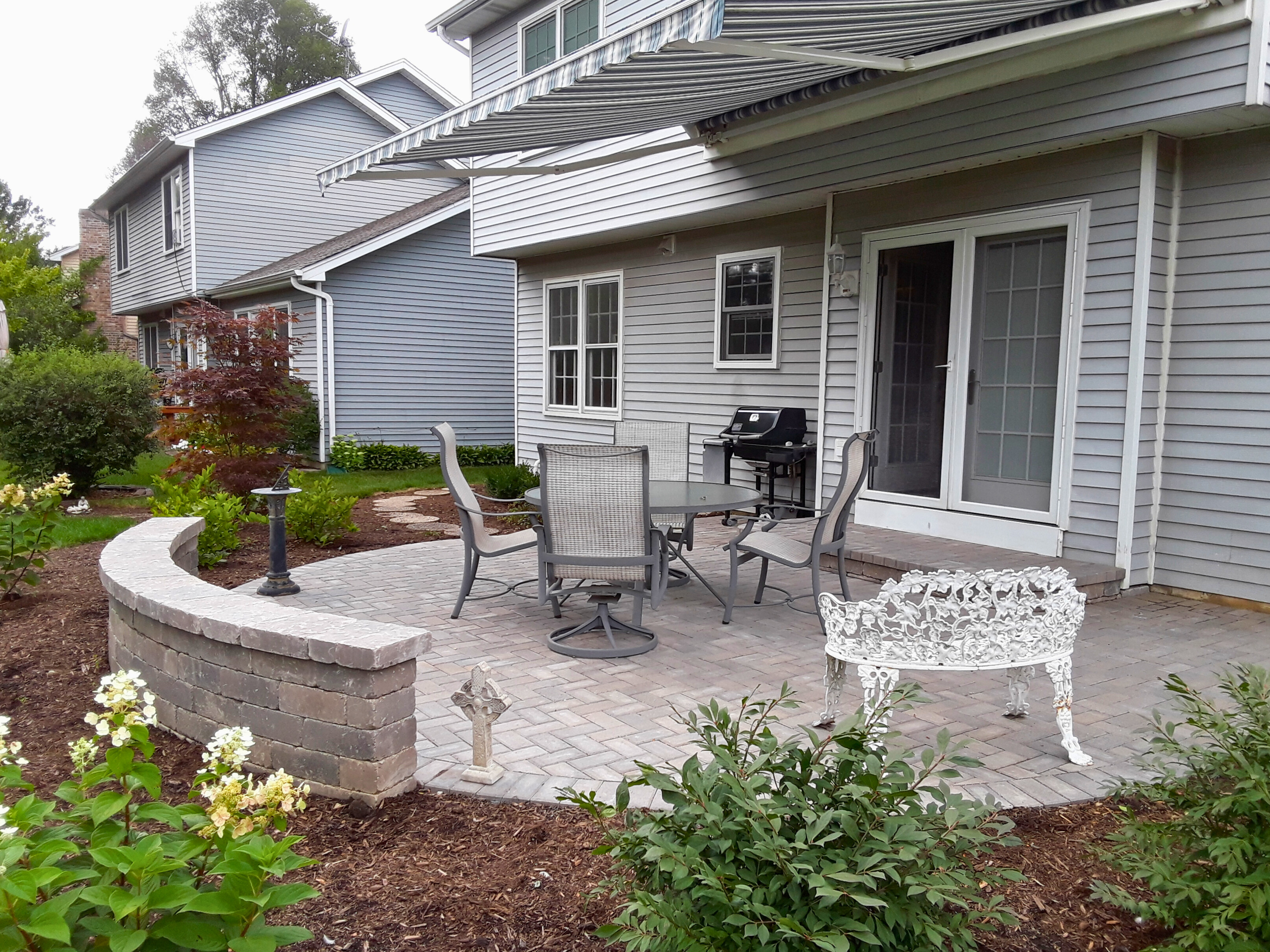 A charming curved paver patio with a low seating wall creates an inviting outdoor retreat for this Wheaton homeowner, offering space for dining and relaxation.