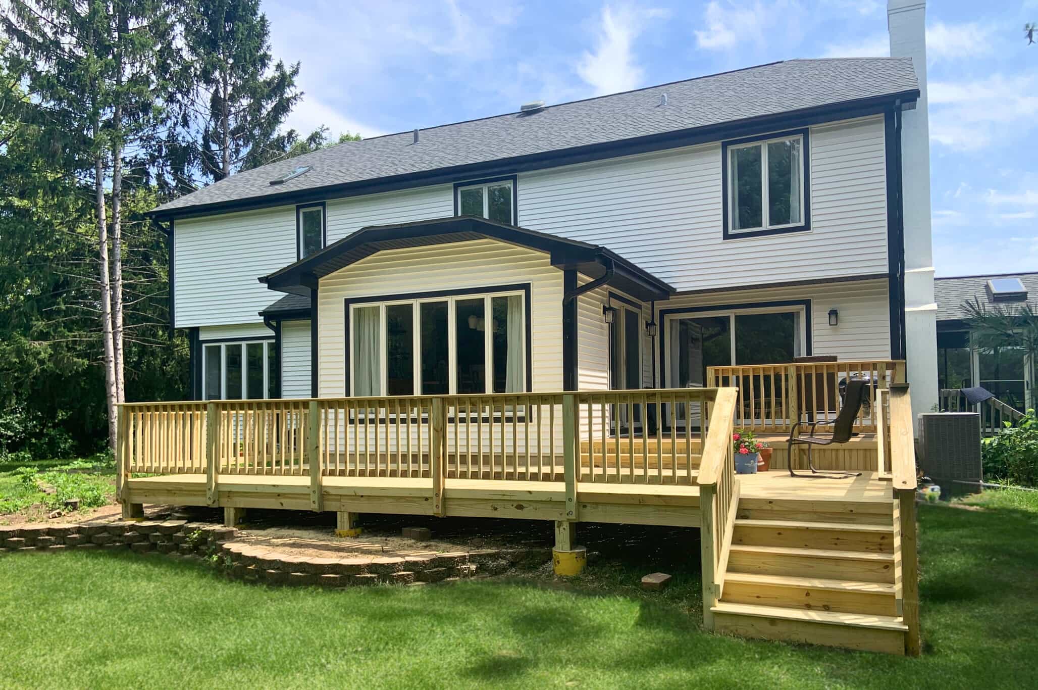 Large, new wooden deck with natural wood railings, attached to a white-sided house with a sunroom, in a backyard setting in St. Charles, IL.