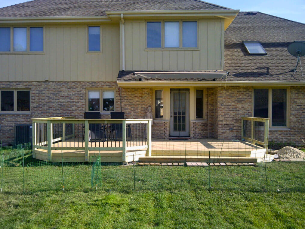 Multi-level wood deck with black metal railings on the back of a brick and tan siding house in Tinley Park, IL.