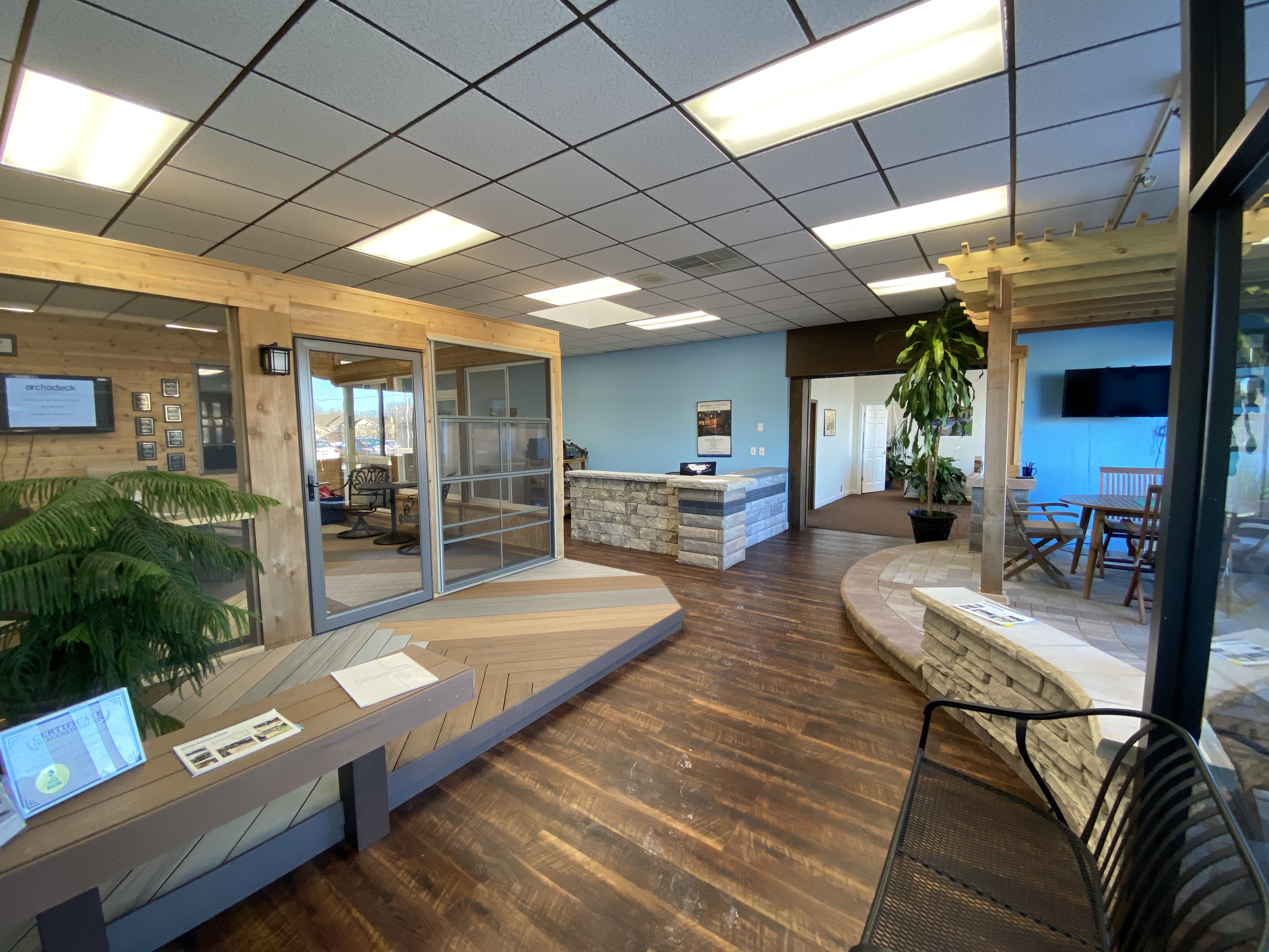 The interior of the Archadeck of Chicagoland showroom, featuring various displays of decking materials, railing options, and outdoor living designs, including a simulated deck area, a seating area, and a reception counter, all well-lit.
