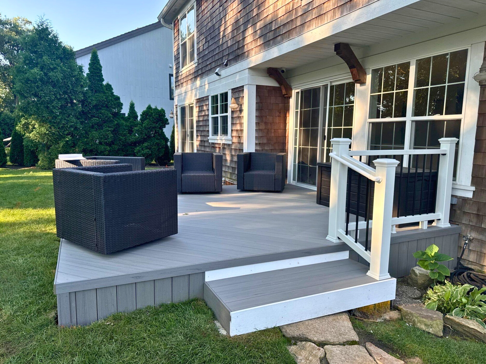 A large elevated wooden deck with black balusters and natural wood railings, featuring a built-in hot tub, attached to a brick home with multiple windows, overlooking a landscaped backyard with lush greenery, under a sunny sky in Lake Forest, IL.