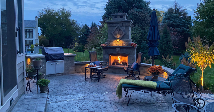 Covered outdoor stone fireplace built with natural veneer stone and wooden pergola posts, creating an outdoor room for Chicagoland homeowner.